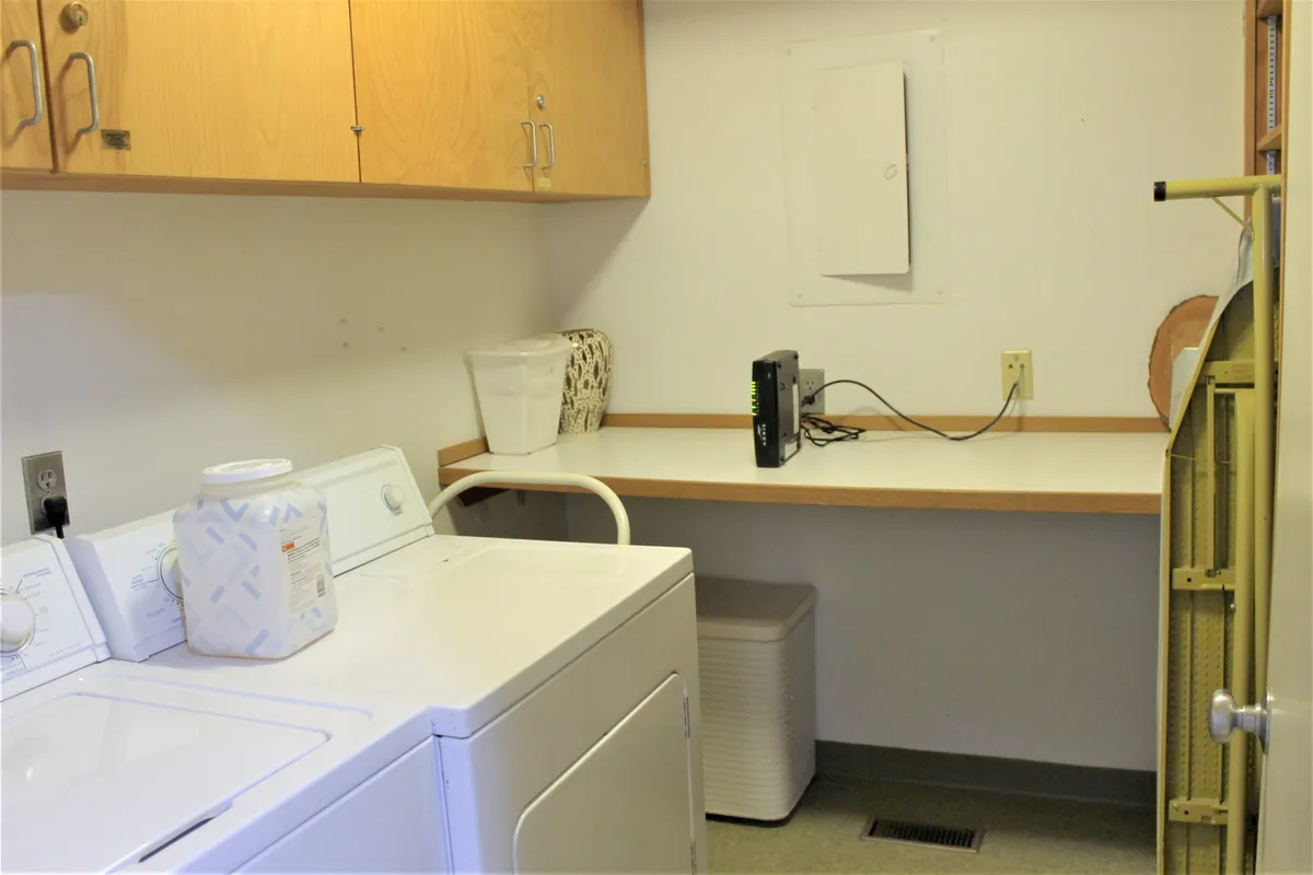 This image features an efficient and tidy laundry area, complete with a washing machine, drying machine, and a well-organized shelf for supplies. The space is functional and bright, conveying the ease of tackling laundry during your stay.
