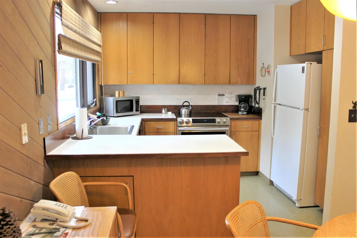 A functional kitchen with a central island, stainless steel appliances, wood cabinets, and bright natural light streaming in. The space is ideal for prepping meals or gathering with family after resort activities.