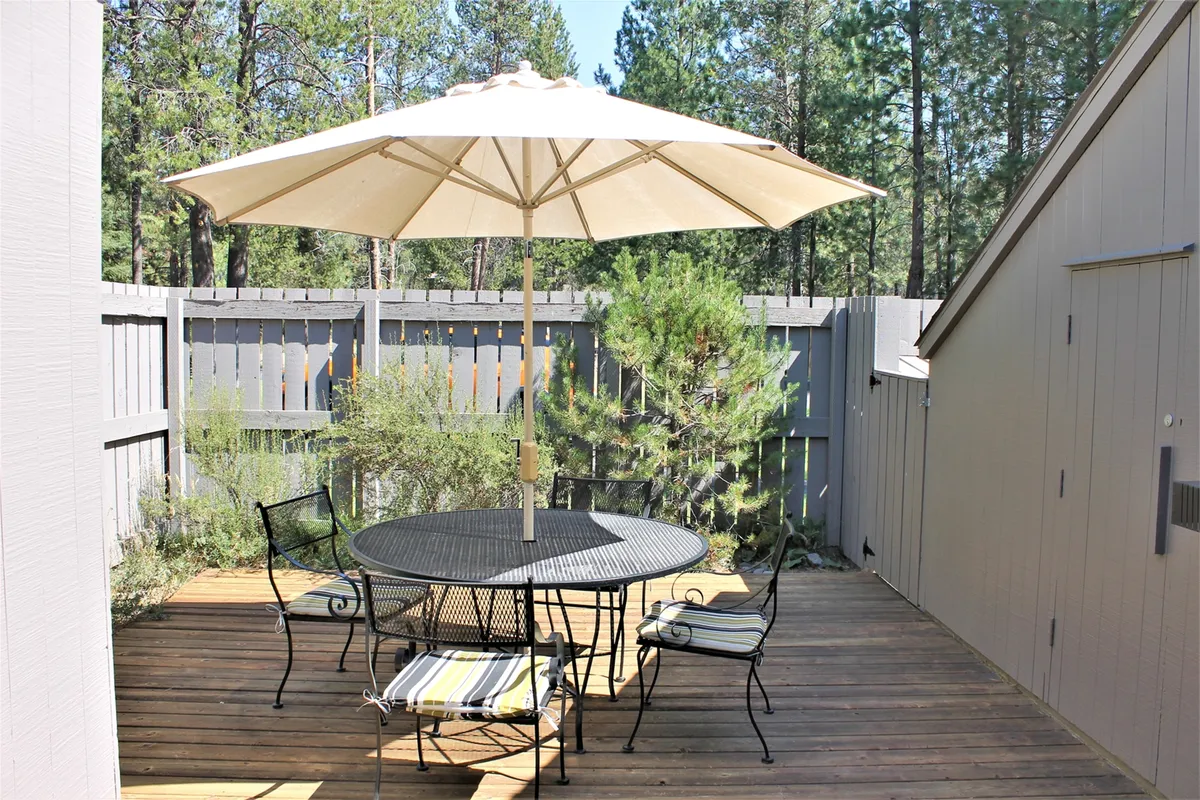 This exterior image showcases a round outdoor table with a parasol set amid lush greenery, suggesting a comfortable patio space ideal for family meals, BBQs, or relaxation after a day of adventures. The inviting setup highlights opportunities for gathering and making memories outdoors.