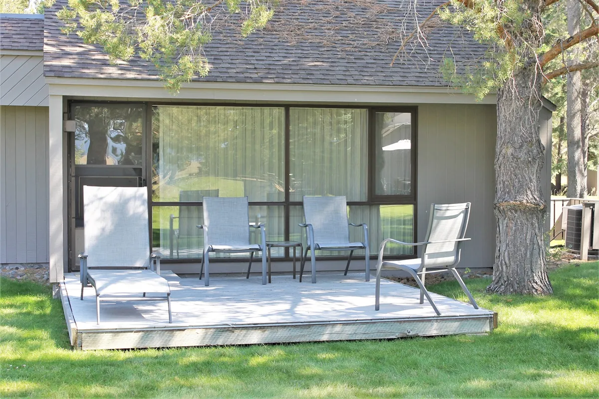 A tranquil patio scene features comfortable seating with large windows behind and lush green grass surrounding the area. The mood is serene, perfect for unwinding, reading, or enjoying time together after a day of activity.