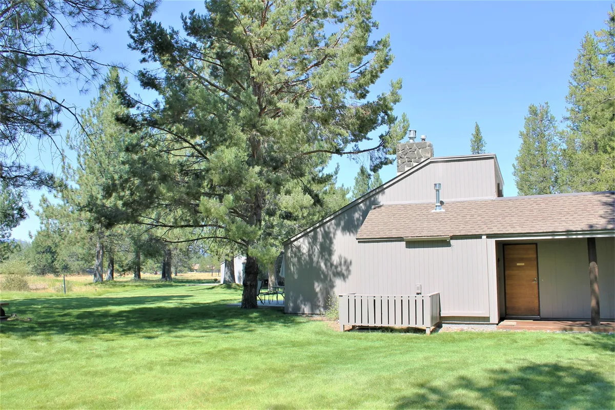 This image features the inviting wooden deck of Meadow House 58, with tall trees providing a serene backdrop. The front door is visible, and the deck is arranged to accommodate outdoor relaxation or al fresco dining. The setting conveys a sense of privacy and connection to the natural surroundings, making it ideal for unwinding or social gatherings.